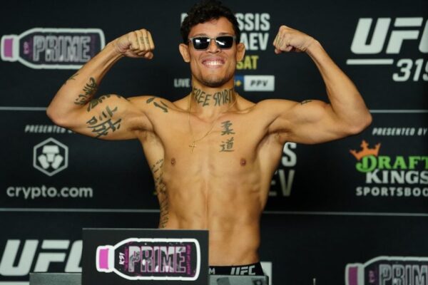 O lutador Caio Borralho sorri e flexiona os bíceps, sem camisa, durante a pesagem oficial do UFC 319.