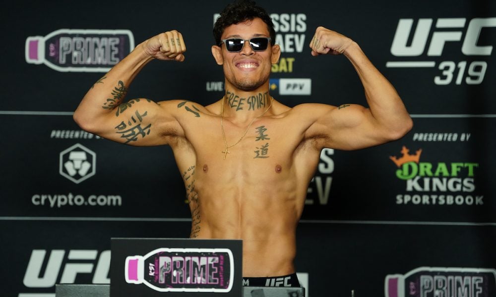 O lutador Caio Borralho sorri e flexiona os bíceps, sem camisa, durante a pesagem oficial do UFC 319.