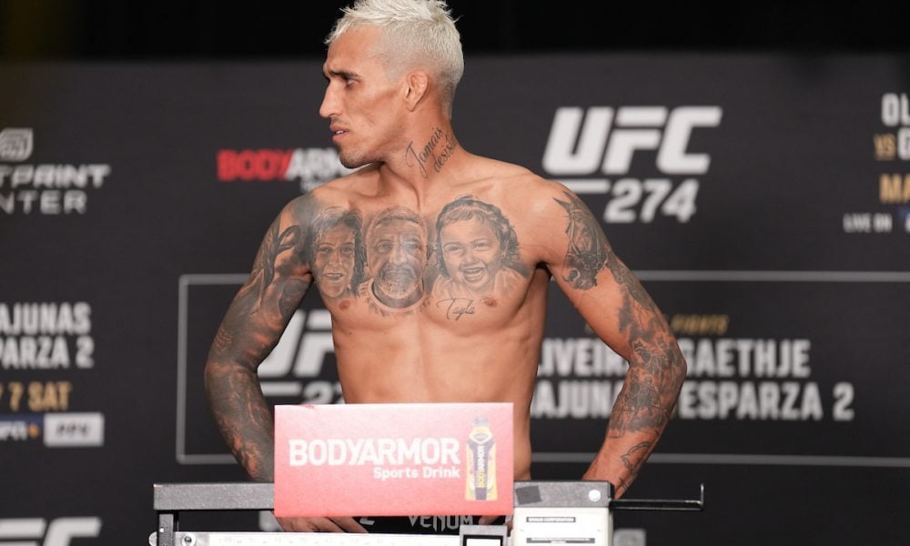 A shirtless, tattooed Charles Oliveira with bleached hair stands on a scale during the official UFC 274 weigh-in.