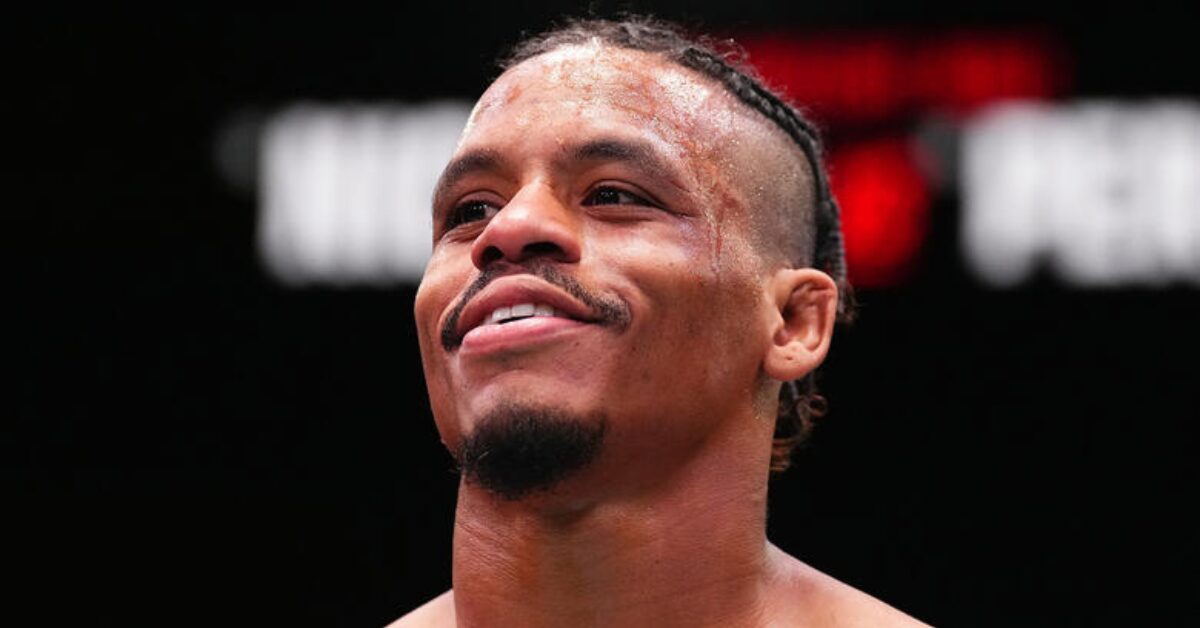 A smiling Black MMA fighter with braided hair and a sweaty forehead looks up.