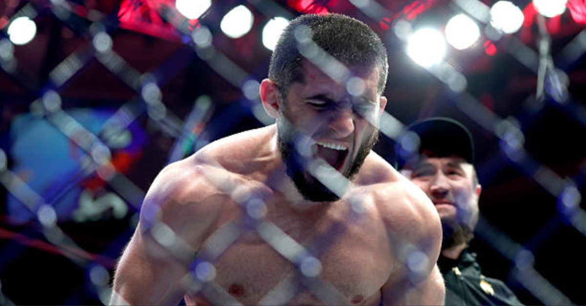 MMA fighter Islam Makhachev roars intensely inside the octagon, seen through the cage fence.