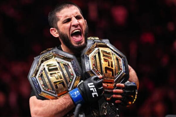 Islam Makhachev, campeão do UFC, grita celebrando com seus dois cinturões de campeão.