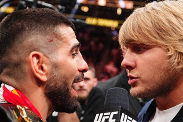 Paddy Pimblett e Ilia Topuria frente a frente no microfone do UFC, em uma encarada tensa.