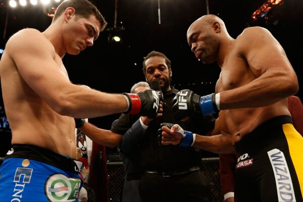 Lutadores do UFC, Anderson Silva e Chris Weidman, se encaram no octógono antes da luta, com o árbitro entre eles.