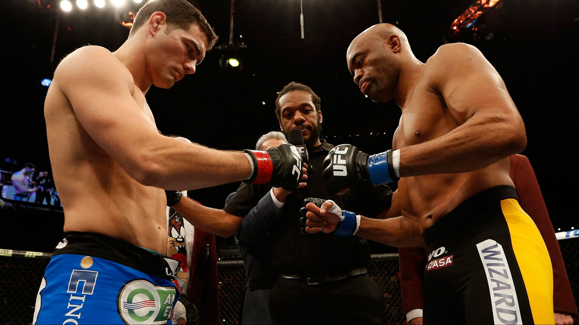 Lutadores do UFC, Anderson Silva e Chris Weidman, se encaram no octógono antes da luta, com o árbitro entre eles.