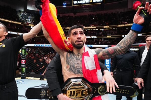 Ilia Topuria, emocionado, celebra o título do UFC com o cinturão, a bandeira da Espanha e uma rosa na mão.