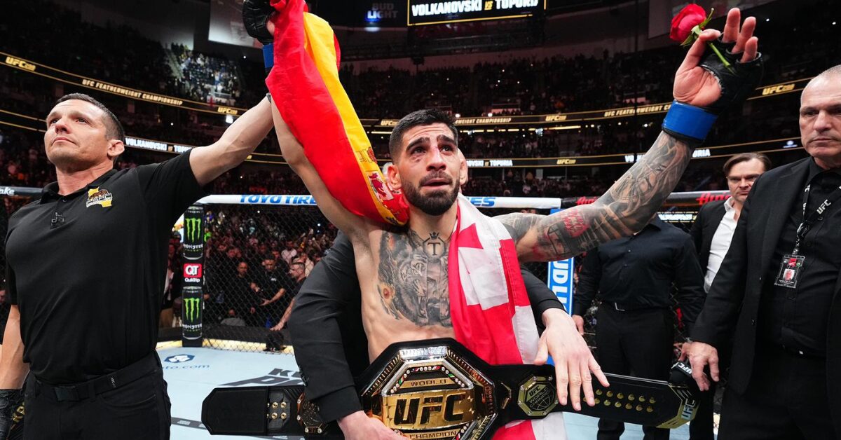 Ilia Topuria, emocionado, celebra o título do UFC com o cinturão, a bandeira da Espanha e uma rosa na mão.
