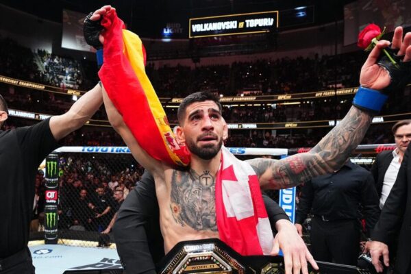 Ilia Topuria, campeão do UFC, comemora emocionado com o cinturão e as bandeiras da Espanha e Geórgia.