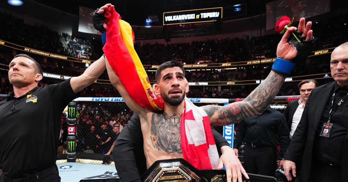Ilia Topuria, campeão do UFC, comemora emocionado com o cinturão e as bandeiras da Espanha e Geórgia.