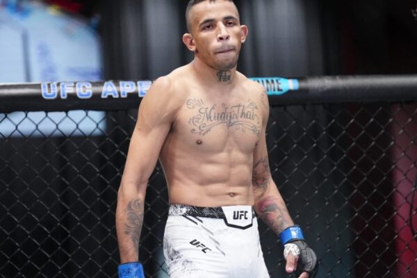 Carlos Prates, lutador do UFC, em pé no octógono, com tatuagem de "Muay Thai" no peito e olhar concentrado.