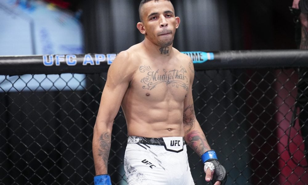 Carlos Prates, lutador do UFC, em pé no octógono, com tatuagem de "Muay Thai" no peito e olhar concentrado.