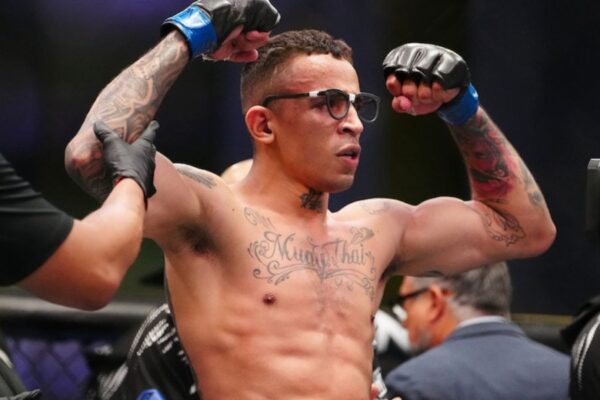UFC fighter Carlos Prates celebrates a win, flexing his tattooed arms and wearing his signature glasses inside the octagon.