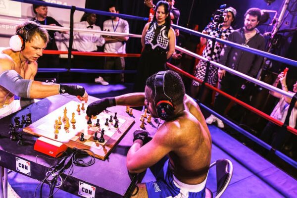Two muscular boxers intensely play chess in a boxing ring during a chess boxing competition.