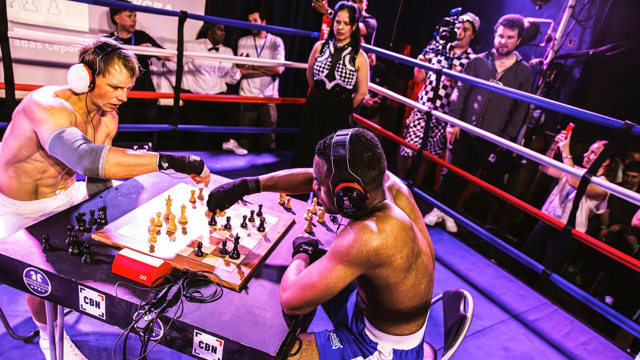 Two muscular boxers intensely play chess in a boxing ring during a chess boxing competition.