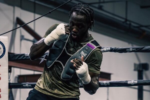 Boxer Terence Crawford trains in a ring wearing an Everlast weighted vest and hand wraps, looking focused and sweaty.