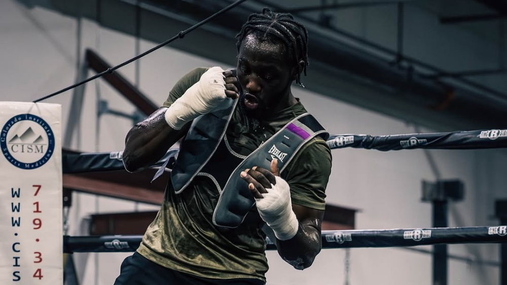 Boxer Terence Crawford trains in a ring wearing an Everlast weighted vest and hand wraps, looking focused and sweaty.