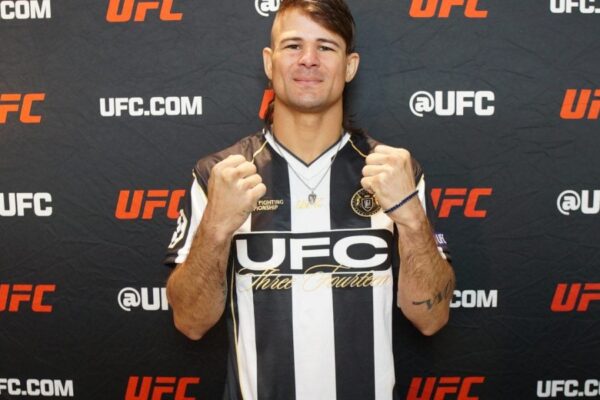 Lutador do UFC Diego Lopes posa com os punhos cerrados, vestindo uma camisa listrada em preto e branco para o media day.