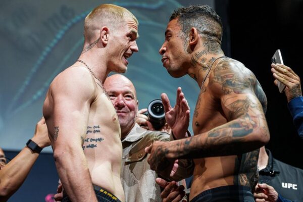 Lutadores do UFC, Ian Garry e Carlos Prates, se encaram na pesagem, com Dana White sorrindo ao fundo.