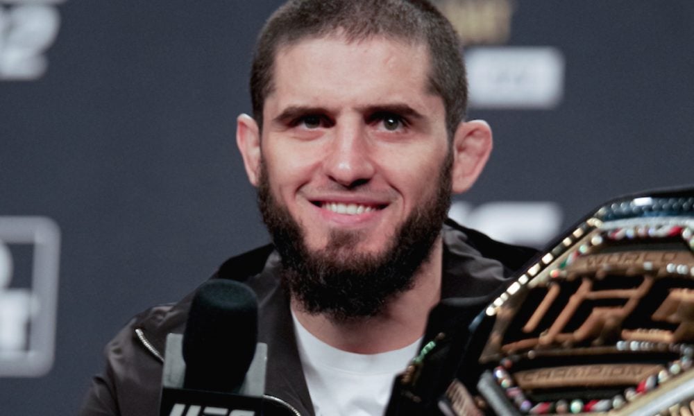 UFC champion Islam Makhachev smiles while holding his championship belt during a press conference.