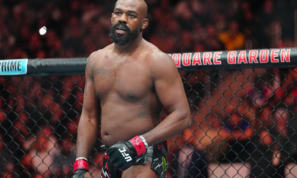 O lutador do UFC Jon Jones, sério dentro do octógono, usando luvas de combate antes de uma luta.