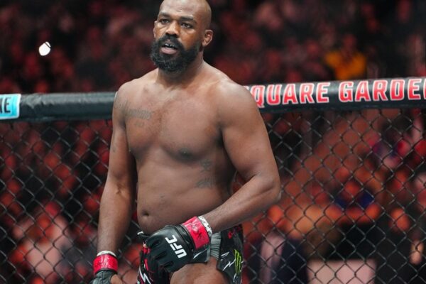 O lutador do UFC Jon Jones, sério e de pé dentro do octógono, com luvas de MMA.