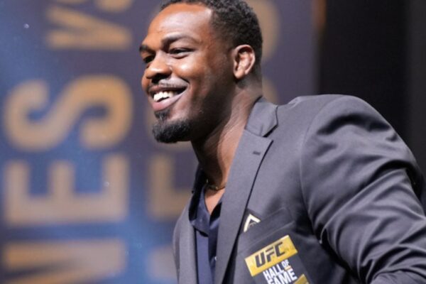 UFC fighter Jon Jones smiles in a suit jacket at his Hall of Fame induction ceremony.