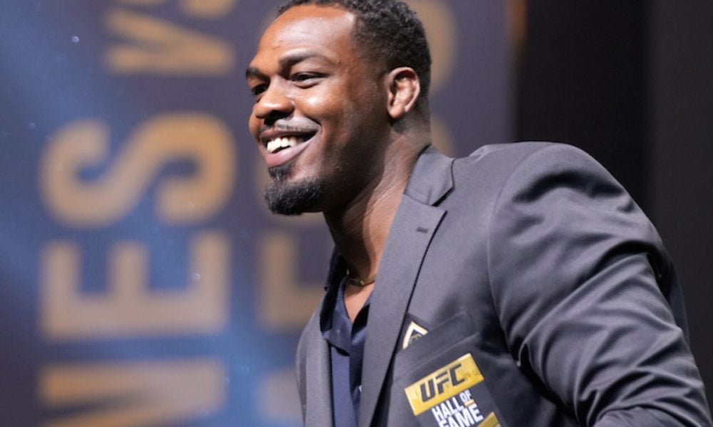 UFC fighter Jon Jones smiles in a suit jacket at his Hall of Fame induction ceremony.