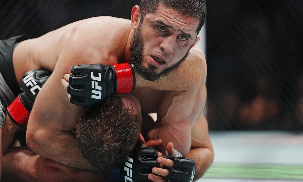 UFC fighter Islam Makhachev intensely applies a chokehold to his opponent on the ground during a match.