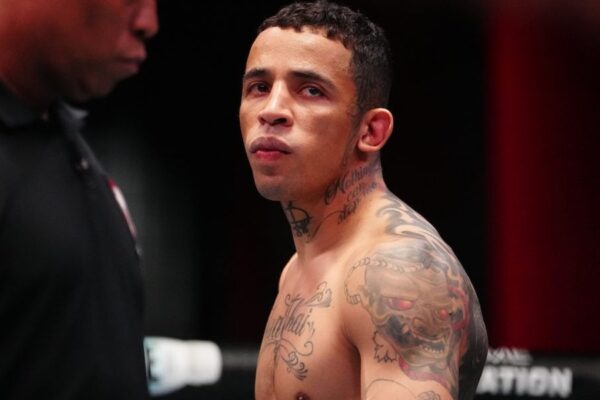 Close do lutador sem camisa e com tatuagens no pescoço e ombro, que encara para o lado com olhar focado.