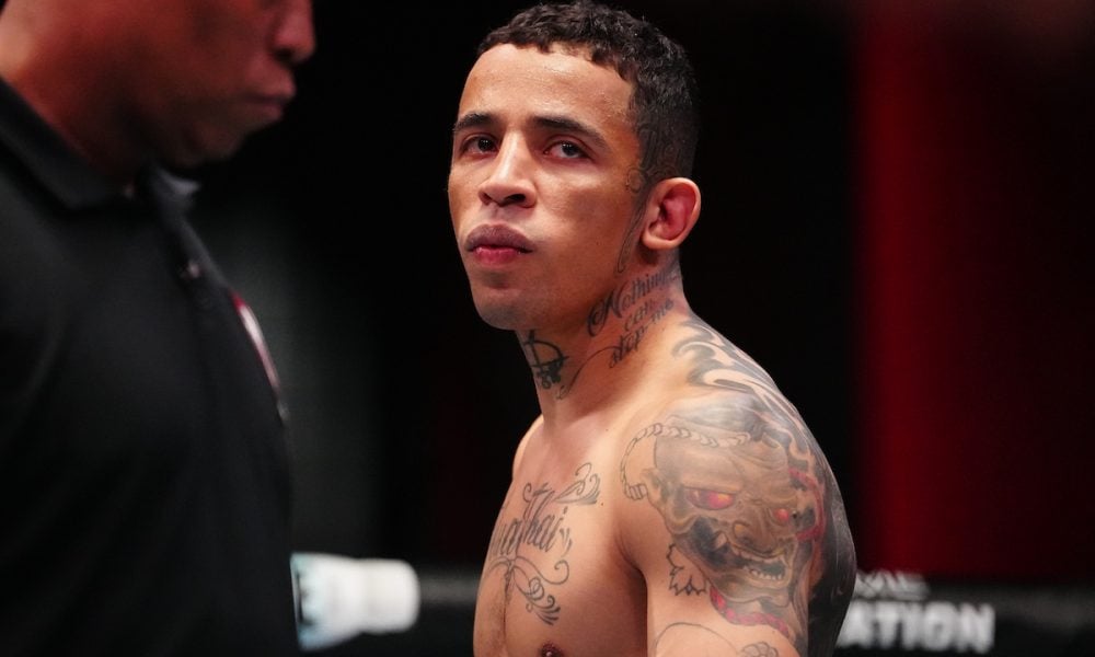 Close do lutador sem camisa e com tatuagens no pescoço e ombro, que encara para o lado com olhar focado.