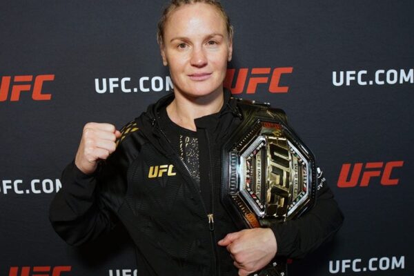Valentina Shevchenko, campeã do UFC, posa com o cinturão no ombro e o punho cerrado para a foto.