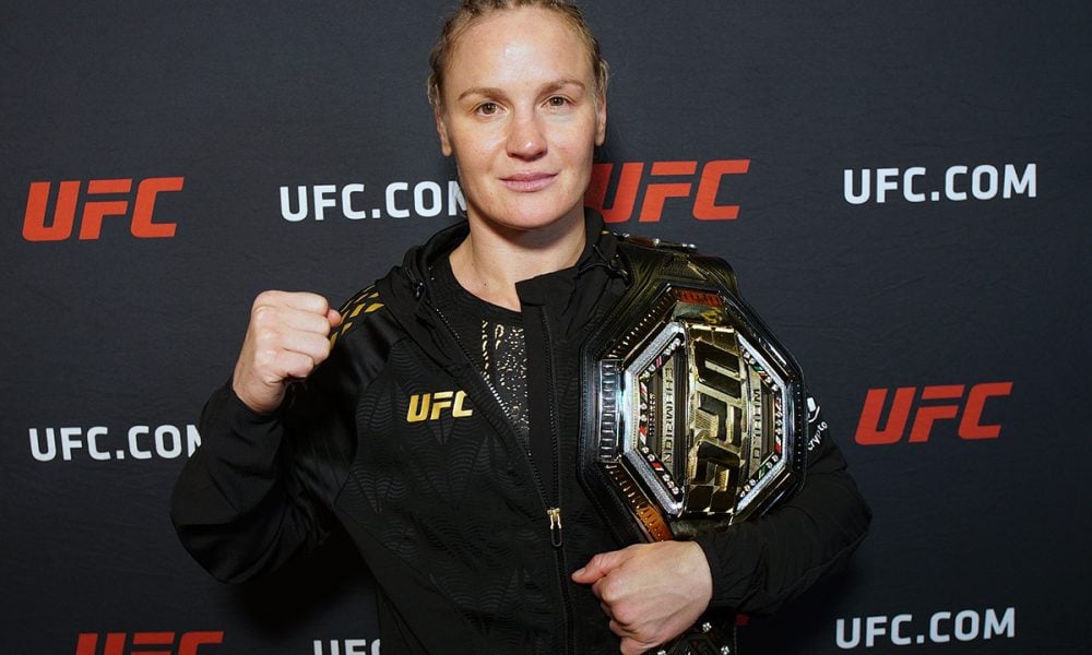 Valentina Shevchenko, campeã do UFC, posa com o cinturão no ombro e o punho cerrado para a foto.