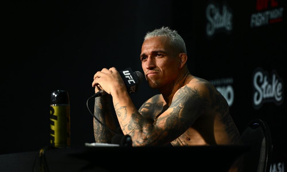Charles do Bronx, lutador do UFC com cabelo platinado, segura um microfone durante uma coletiva de imprensa.