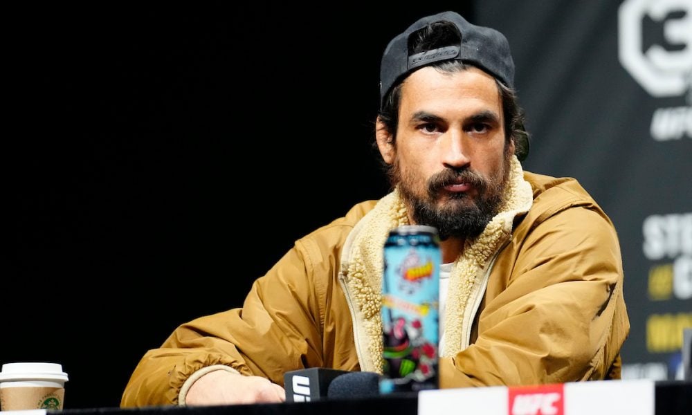 O lutador Kron Gracie, de boné e jaqueta, encara a câmera durante uma coletiva de imprensa do UFC.