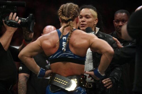 Amanda Nunes encara Kayla Harrison no octógono do UFC. Harrison, de costas, ostenta o cinturão de campeã.