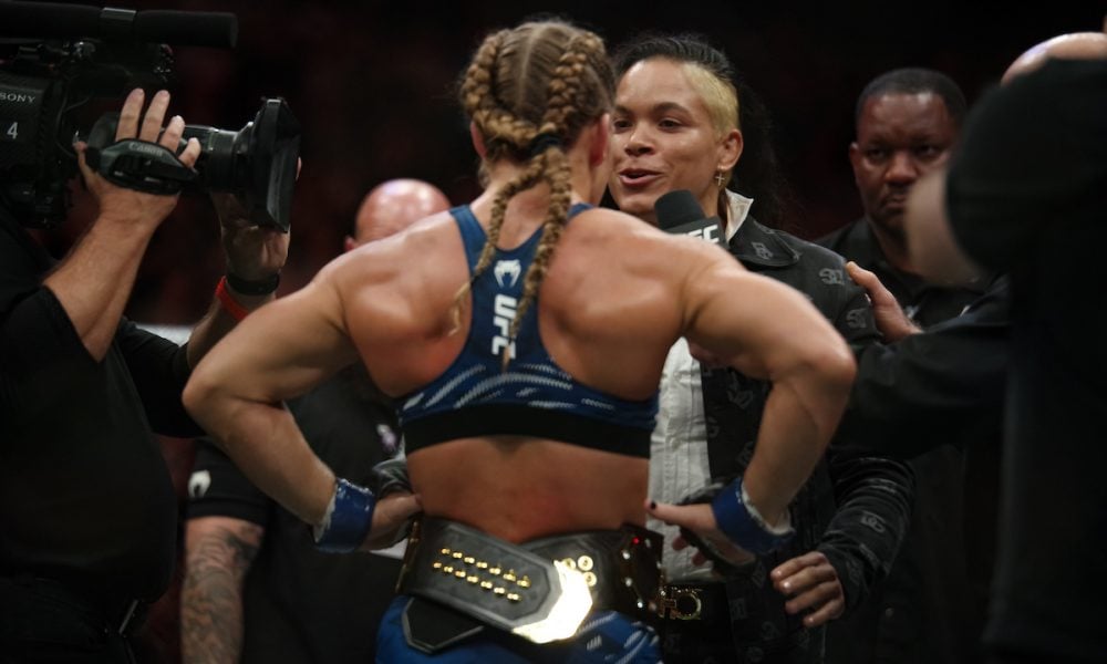 Amanda Nunes encara Kayla Harrison no octógono do UFC. Harrison, de costas, ostenta o cinturão de campeã.