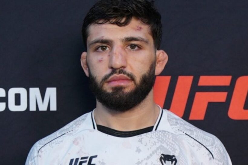 O lutador do UFC Arman Tsarukyan posa sério, com o rosto machucado, em frente a um painel do evento.