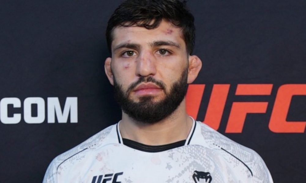 O lutador do UFC Arman Tsarukyan posa sério, com o rosto machucado, em frente a um painel do evento.