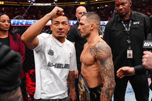 Lutador com punho erguido encara o campeão do UFC com cinturão e tatuagens, dentro do octógono.