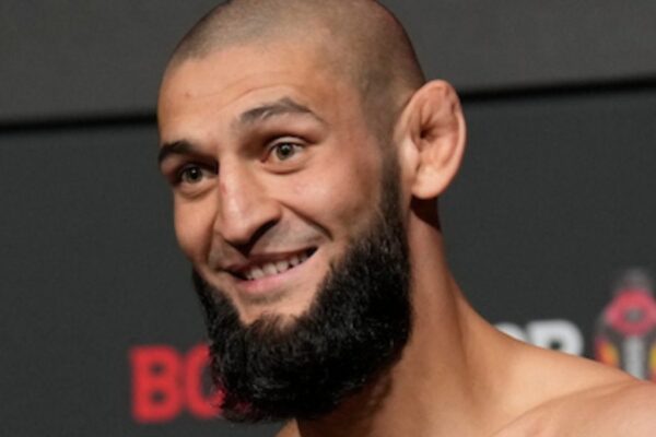 Lutador do UFC Khamzat Chimaev sorri em close-up, com barba cheia e cabeça raspada.