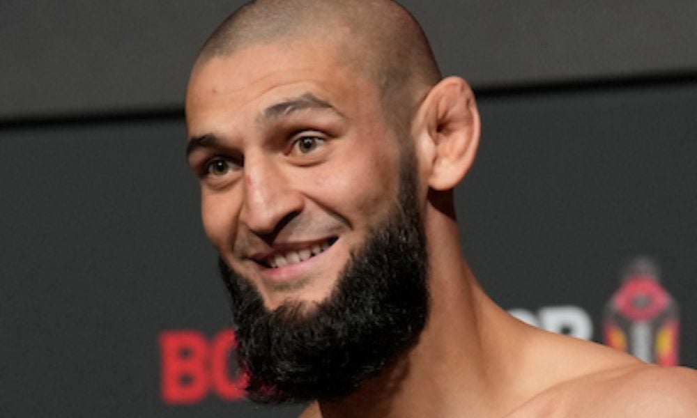 Lutador do UFC Khamzat Chimaev sorri em close-up, com barba cheia e cabeça raspada.